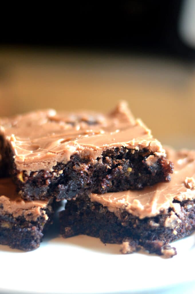 a photo of 3 zucchini brownies that look fudgy with a thin layer of frosting on top.
