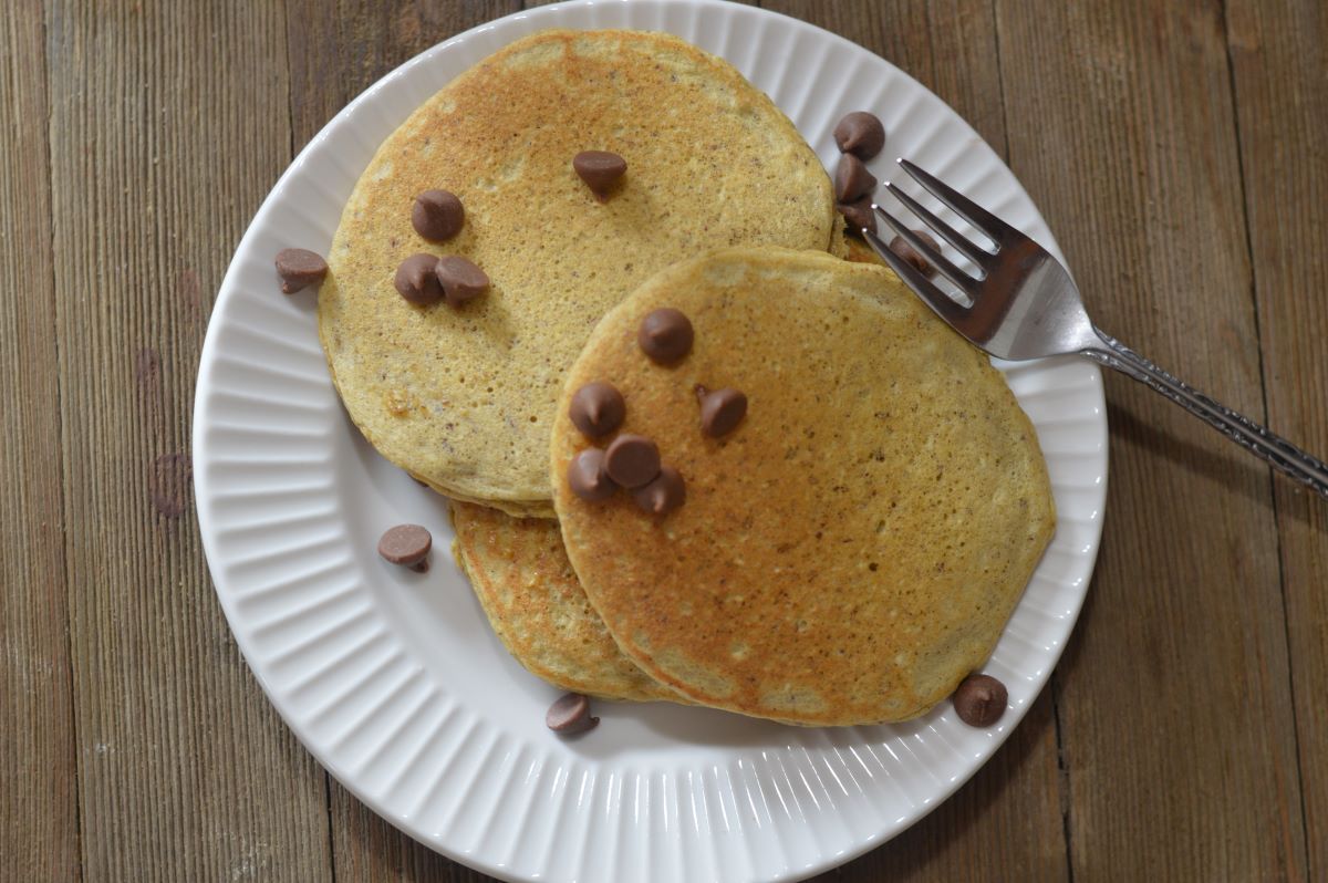 2 pancakes with chocolate chips sprinkled on top. On white plate with fork.