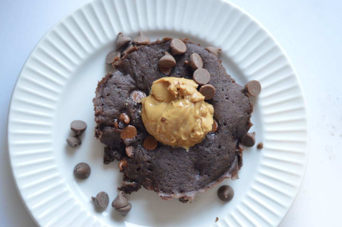 Picture of chocolate mug cake on white plate. Dollop of peanut butter on top with chocolate chips.