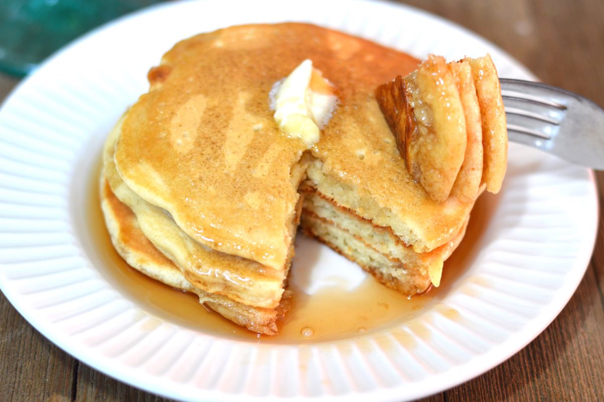 Picture of 3 pancakes stacked on white plate with syrup and butter on top. 