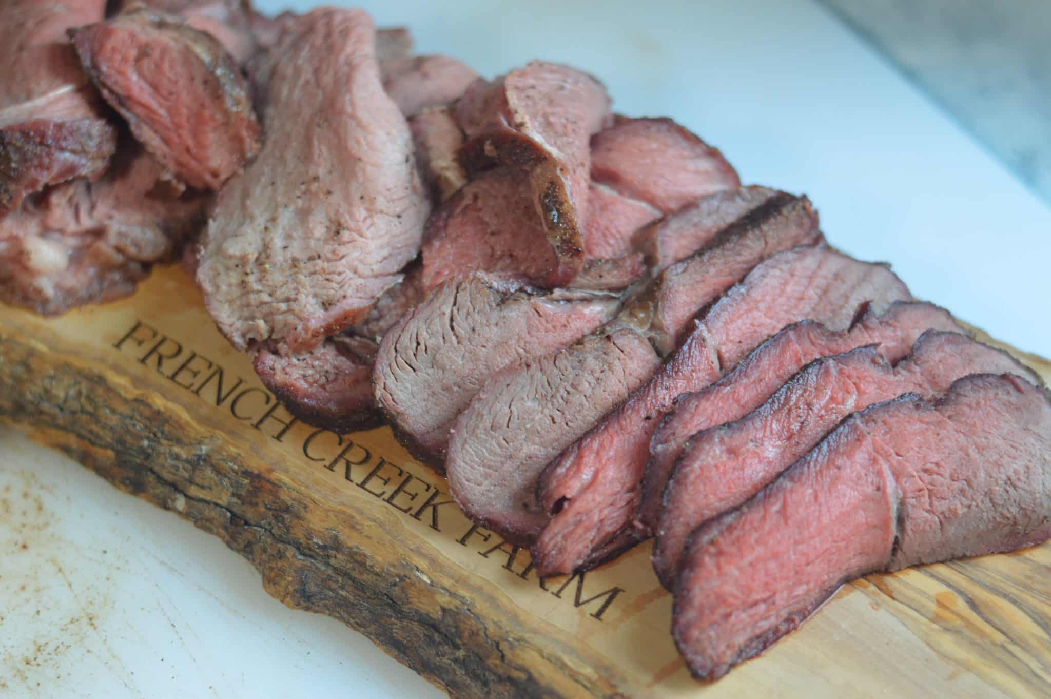 Sliced sirloin tip roast from smoker arranged on a board that says “French creek farm”