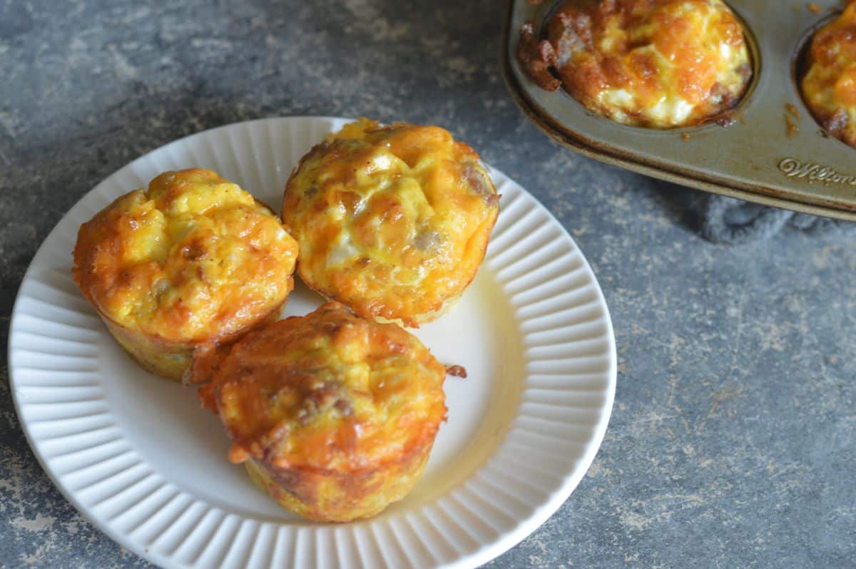 3 sausage egg and cheese Muffins arranged on a white plate. A corner of the muffin tin.