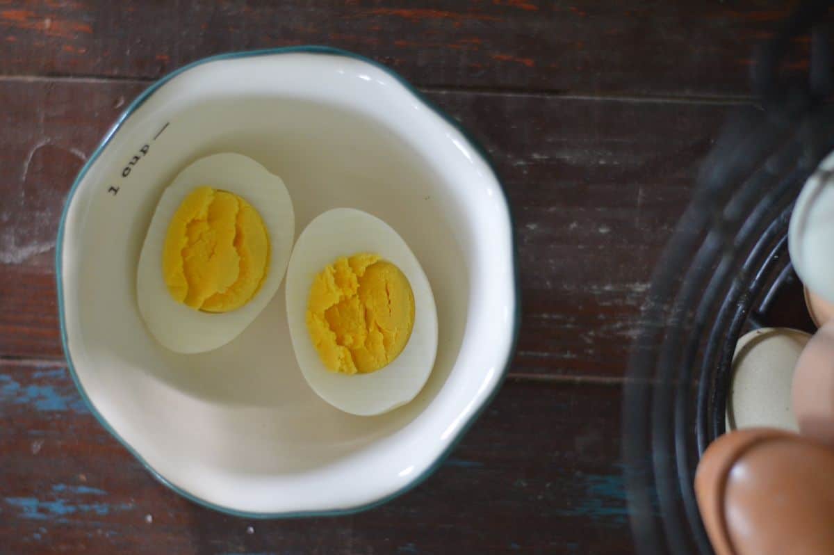 A photo of a hard boiled egg (farm fresh) cut open next to a basket of colorful eggs 