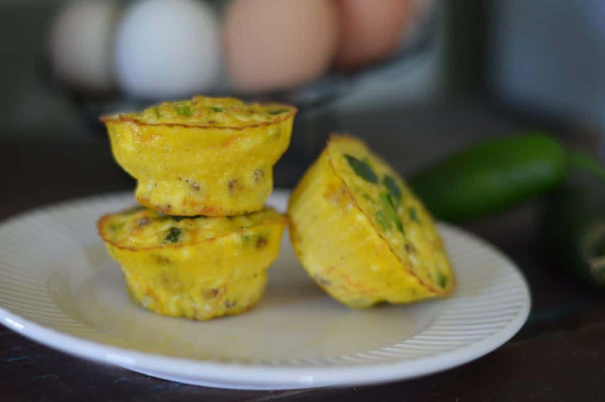 3 egg Jalepeno Popper Egg bites on a white plate. Two egg bites stacked and one leaned up against.